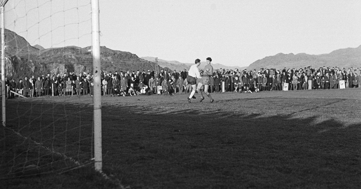 Fotografía antigua en blanco y negro de un partido con la grada llena y montañas al fondo