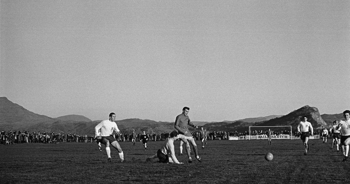 Fotografía antigua en blanco y negro de un partido con montañas al fondo