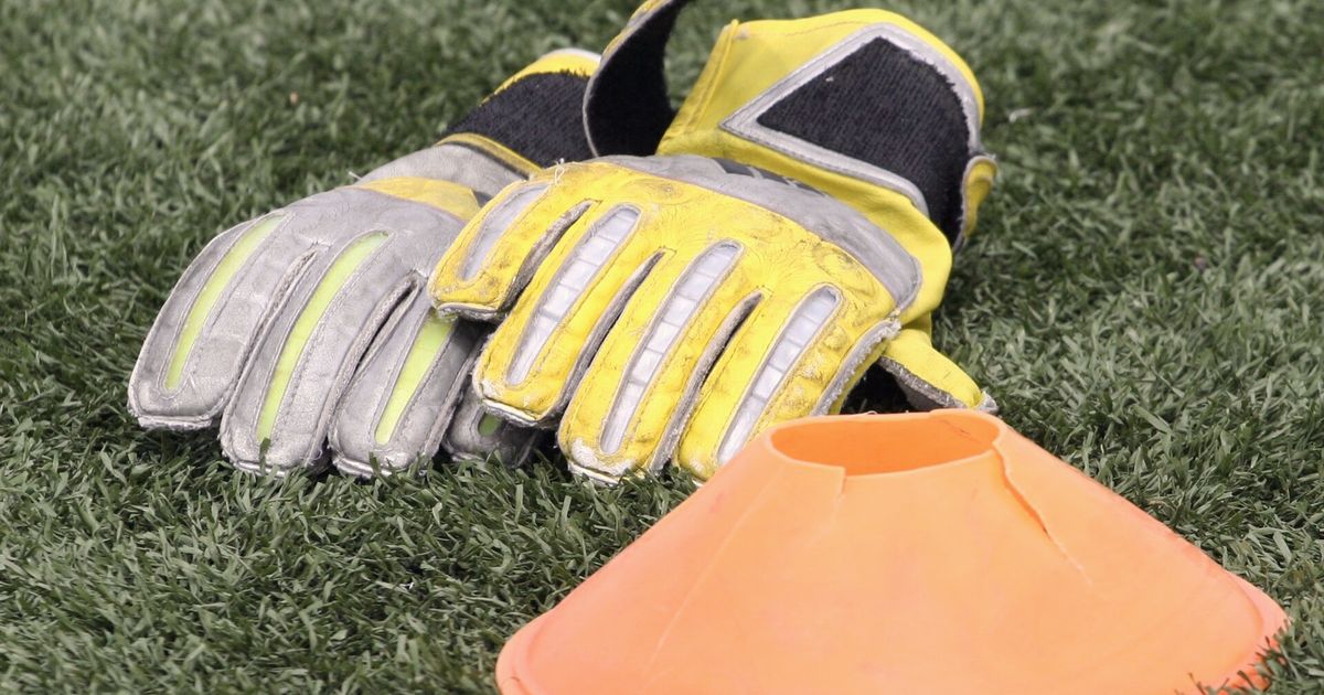 Guantes de portero y un cono naranja sobre el césped