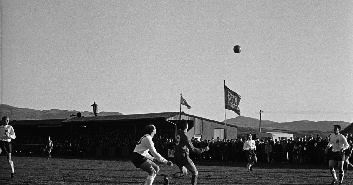 Fotografía antigua en blanco y negro de un partido, con el balón en el aire y la grada llena